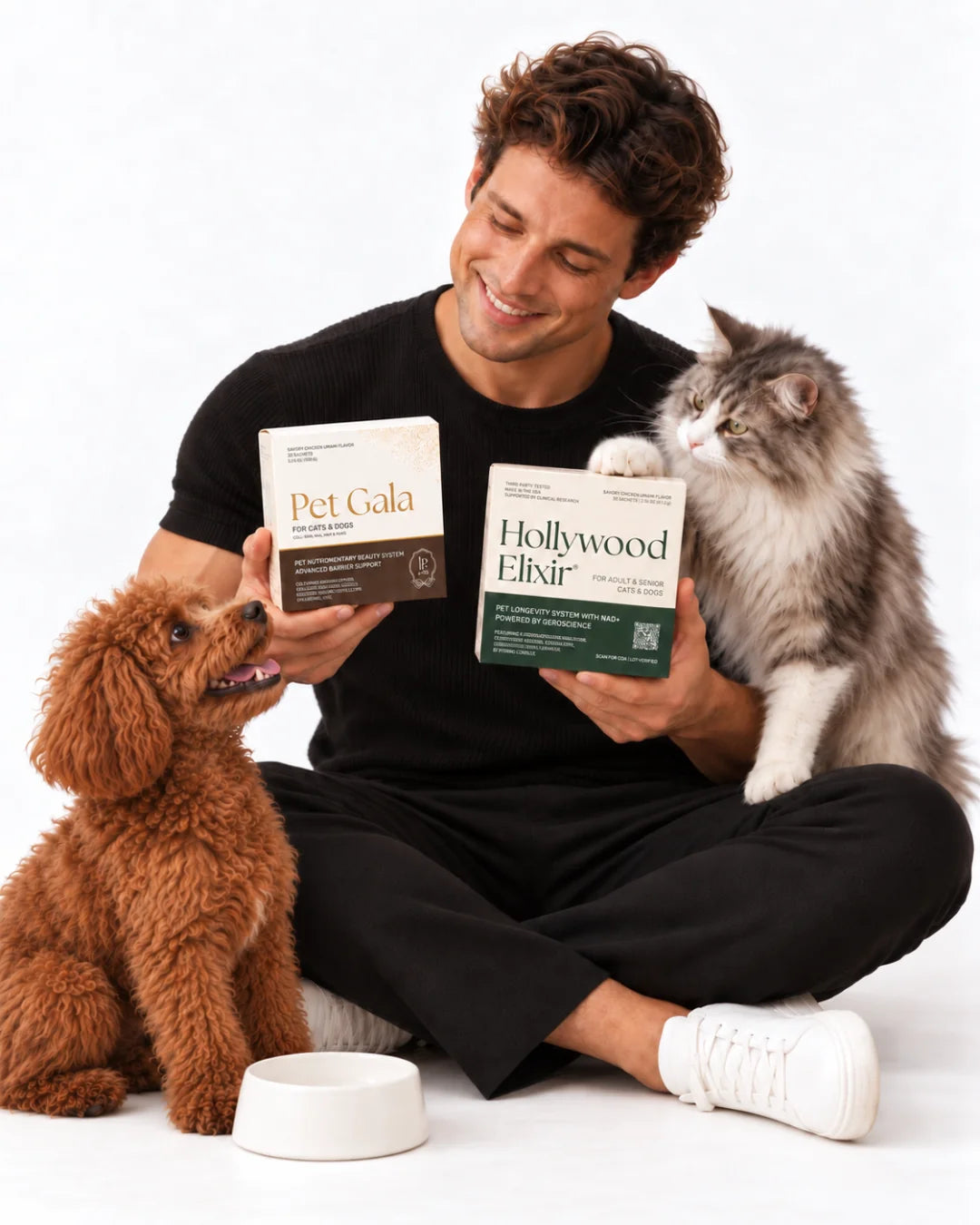 A smiling man holding Pet Gala and Hollywood Elixir boxes with a poodle and a long-haired cat
