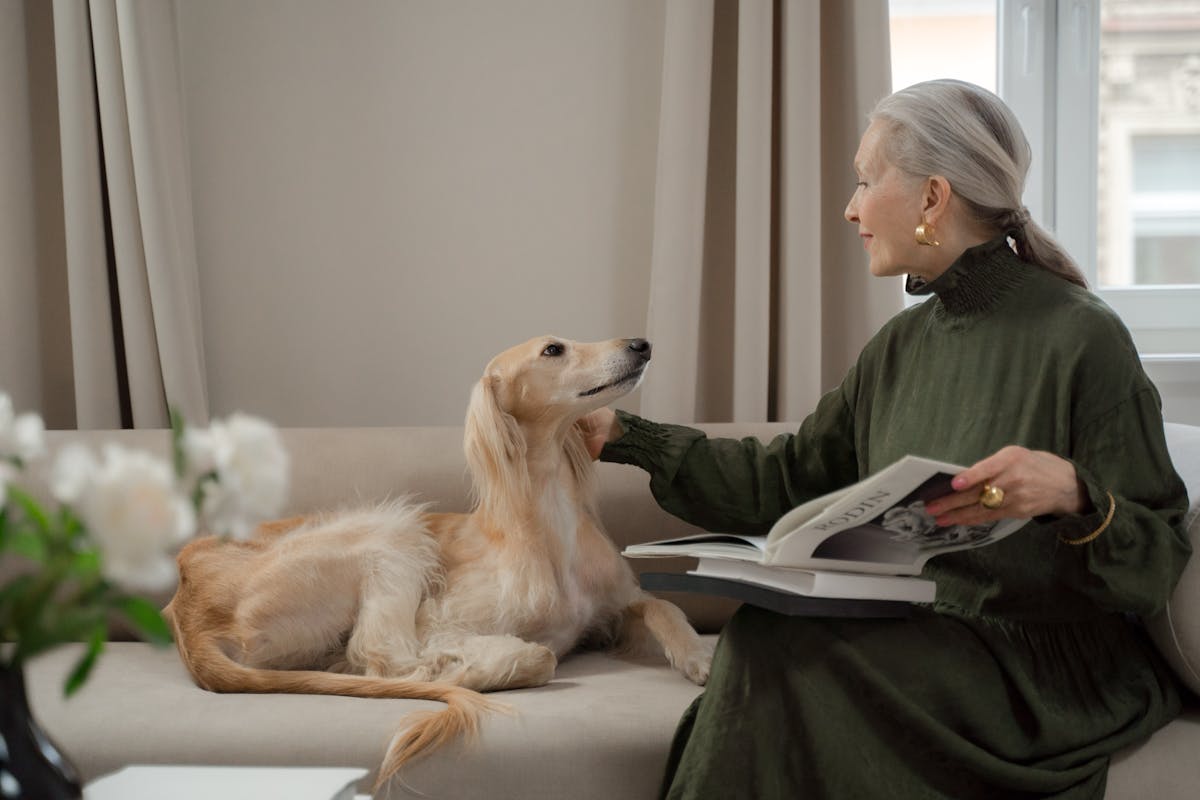 Elegant senior woman reading with a Saluki dog on a living room sofa.