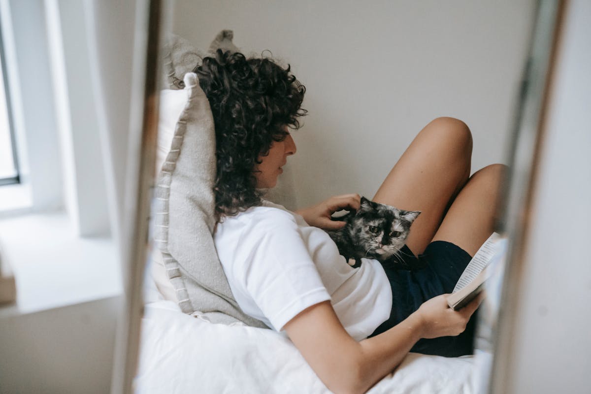 Woman relaxing with a cat and book in a cozy bedroom setting, exuding warmth and comf — Senior Pets and Multi-System Support