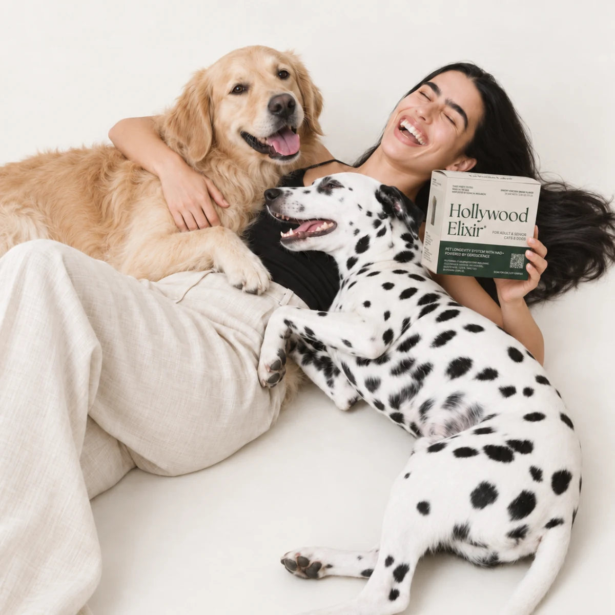 A laughing woman reclining with a golden retriever, a Dalmatian and Hollywood Elixir