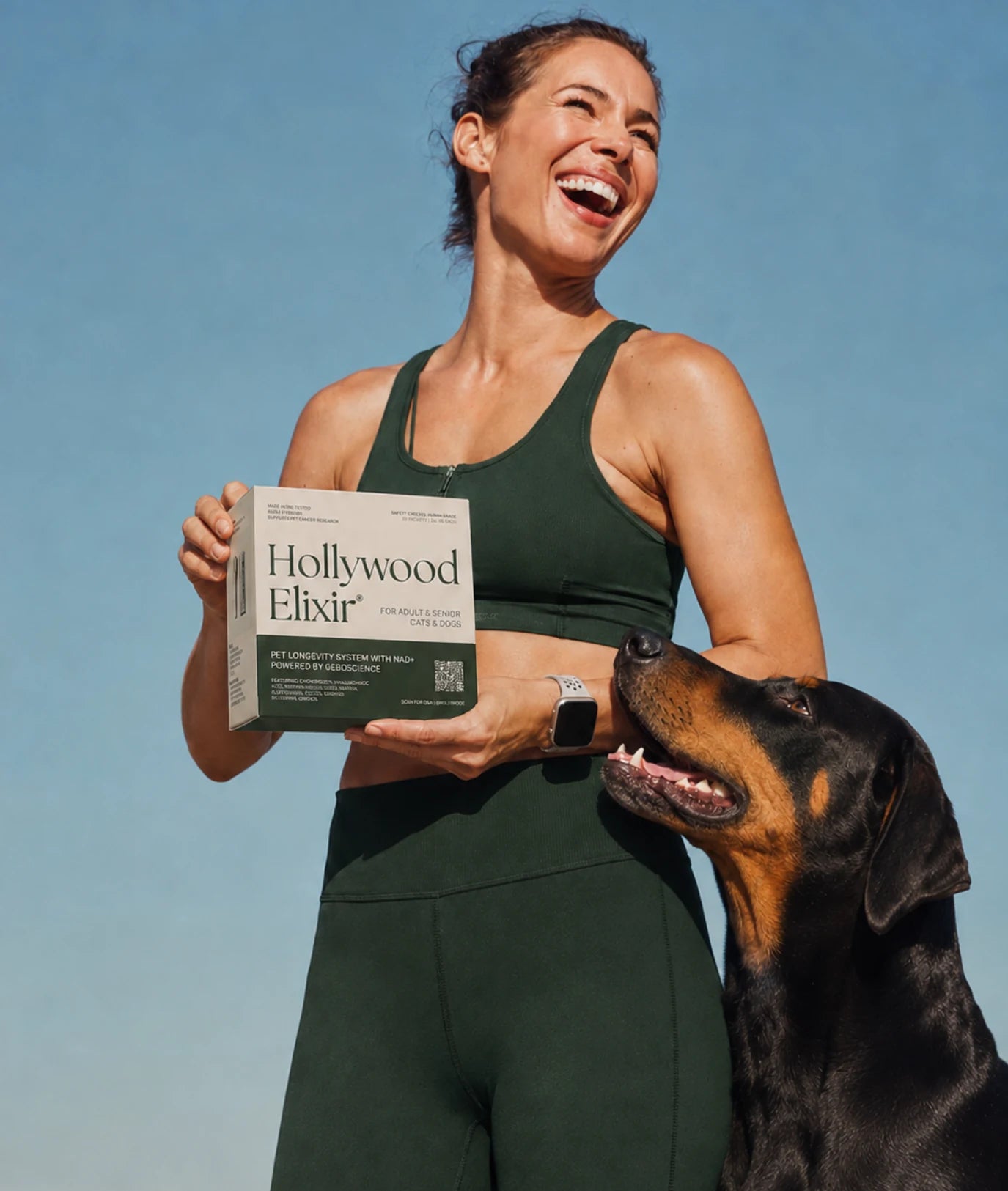A woman holding Hollywood Elixir with her dog beneath a blue sky