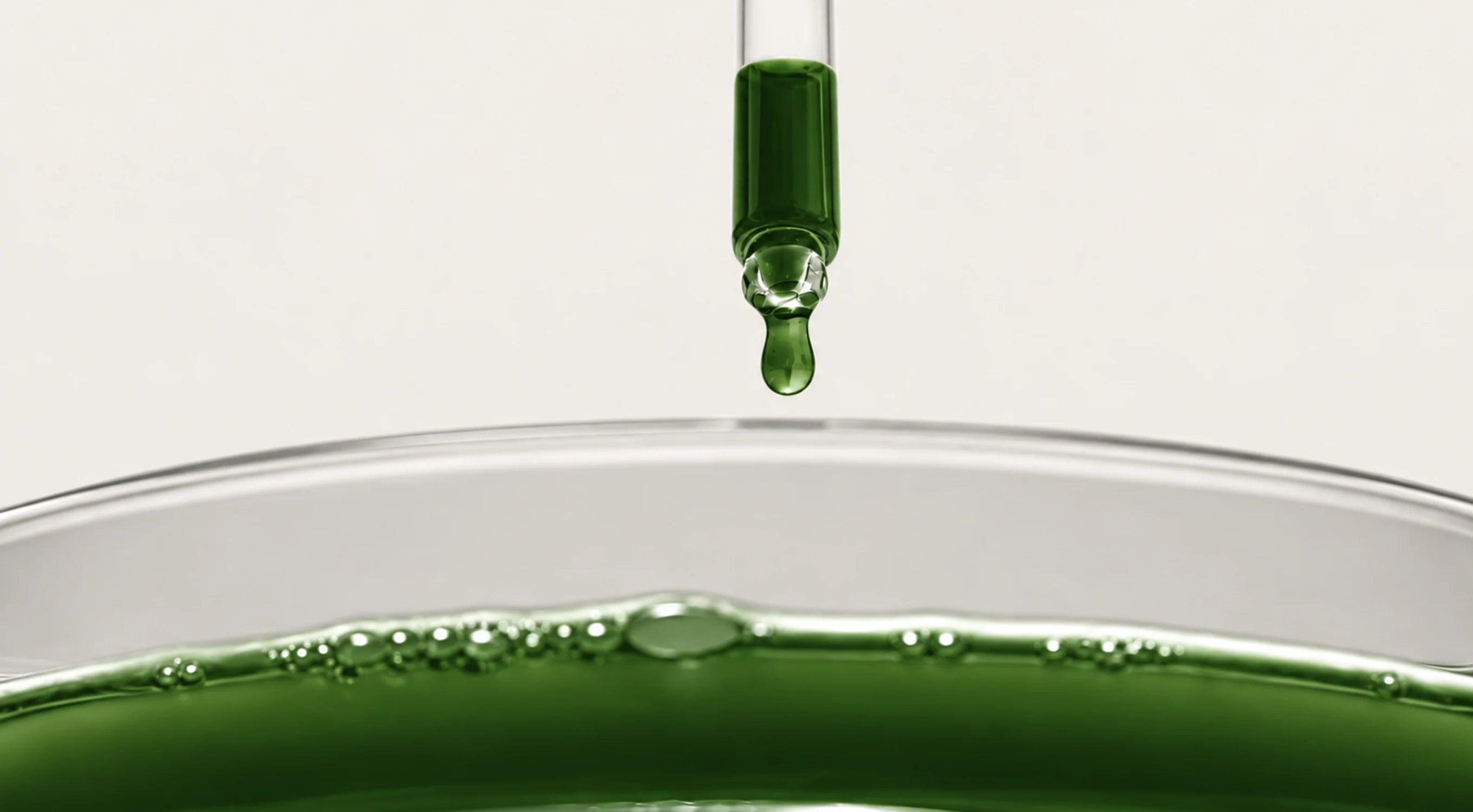 A glass dropper releasing a green droplet into a dish