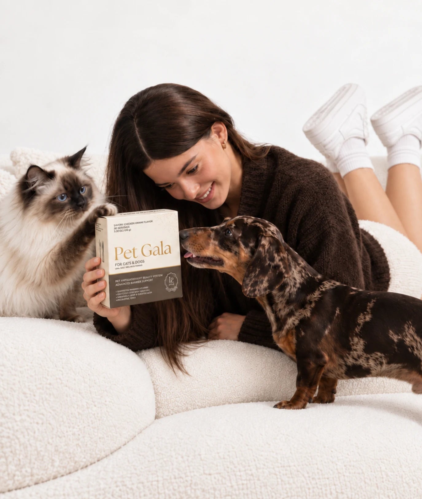 A woman holding Pet Gala with her cat and dachshund on a white blanket