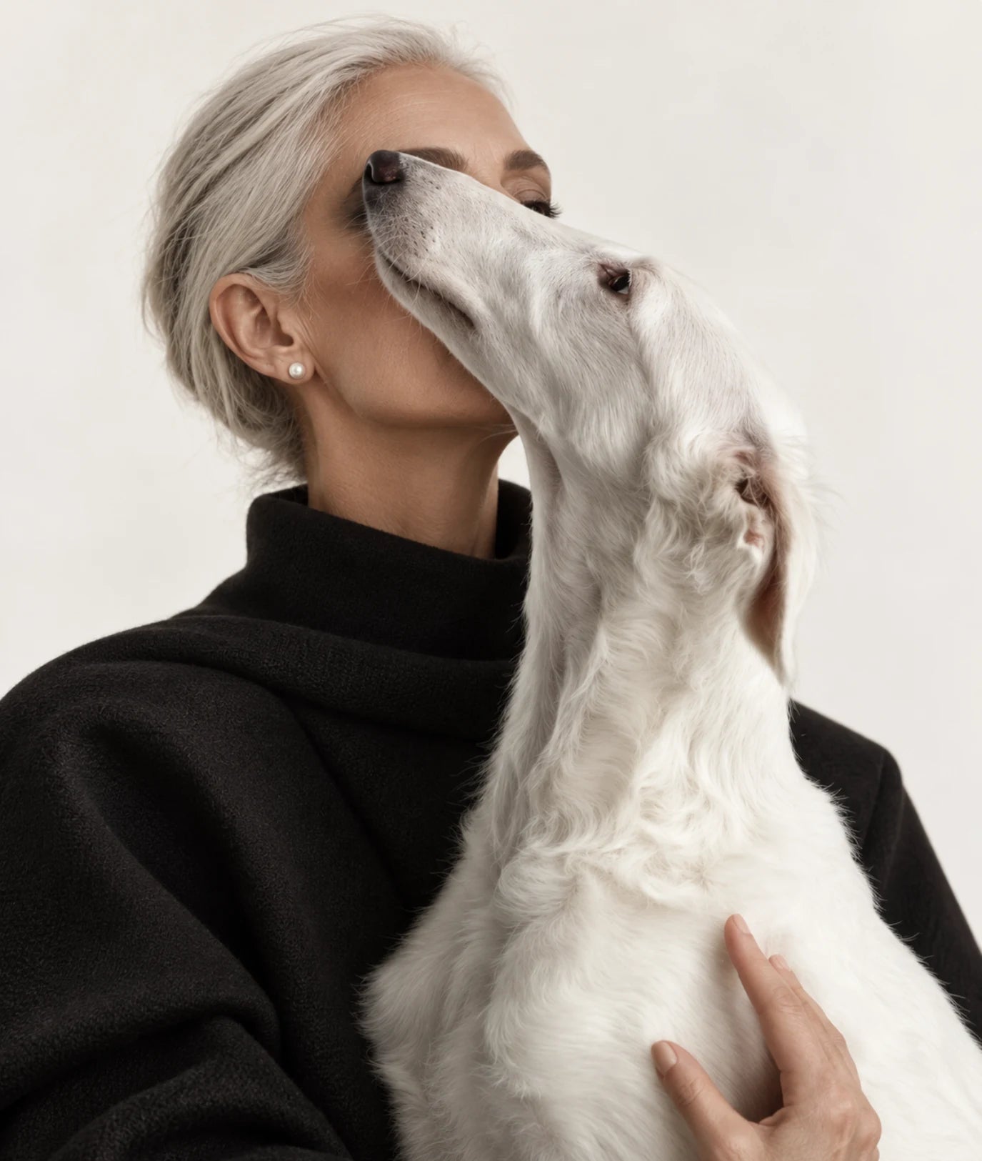 A white sighthound resting its head against a woman in black